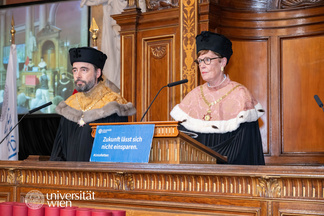Foto von der Abschlussfeier, die am 27.5. zeitgleich mit der großen unisretten Demonstration stattgefunden hat. Am Foto zu sehen sind die Dekanin der Katholisch-Theologischen Fakultät Andrea Lehner-Hartmann sowie Assoz. Prof. Ioan Moga. Am Pult steht eine Tafel mit der Aufschrift "Zukunft lässt sich nicht einsparen".