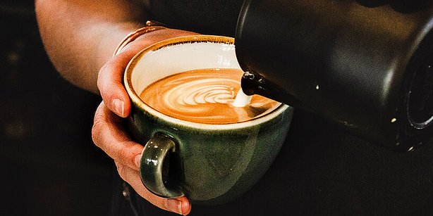 Eine Hand hält eine Tasse, in die Kaffee eingeschenkt wird.