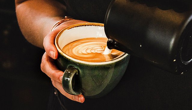 Eine Hand hält eine Tasse, in die Kaffee eingeschenkt wird.