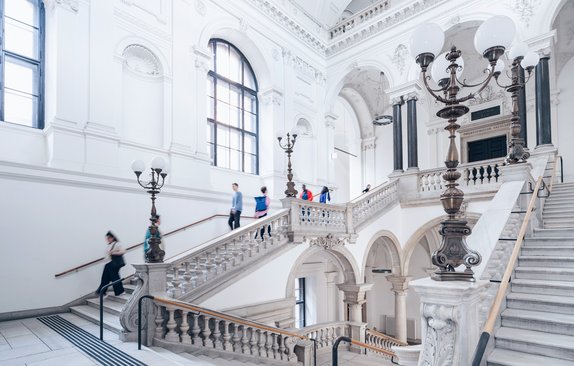 Personen gehen die große Treppe im Hauptgebäude der Universität Wien hinauf und hinunter.